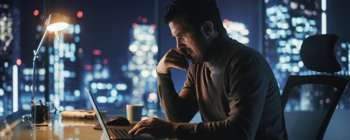 Portrait of Thoughtful Successful Businessman Working on Laptop Computer in His Big City Office at Night. Energetic Digital Entrepreneur does Data Analysis for e-Commerce Strategy.